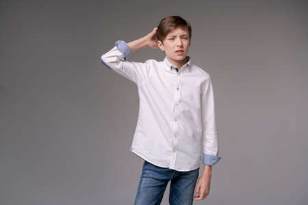 Thoughtful young teen man holding hand on chin indecision pose in white shirtisolated on gray studio background, considering making difficult feelings of doubt in FreeSpace text conceptの写真素材