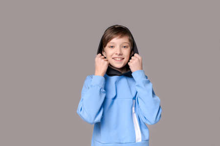 Positive studio portrait cute toothy smiling young caucasian guy isolated on gray copy space. Happy teenager wearing a blue sweatshirt looking at the camera. Cheerful guy gesturing cheerfullyの写真素材
