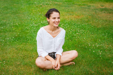 Young woman seated enjoy rest and relax merrily laughing with happiness while sitting on green grass in the park on the lawn. Caucasian girl enjoys a day off in natureの写真素材