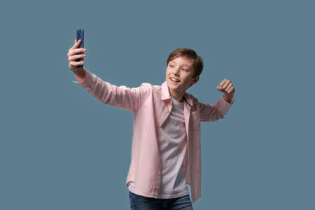 Young handsome man teenager communicates by smartphone video communication over blue background in...