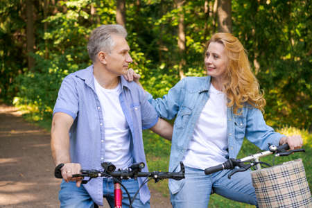 Active old age, people and lifestyle concept happy senior couple riding bicycles in summer park on a sunny day in casual comfortable clothes, enjoy life and time spent togetherの写真素材