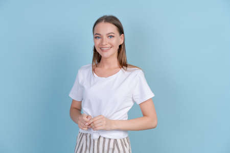 Portrait young beautiful woman in white t-shirt with crossed arms. Confident and successful girl, pretty millennial Caucasian female model with long hair isolated on blue studio backgroundの写真素材
