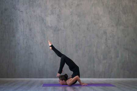 Side view portrait beautiful young woman wearing black sportswear, exercising against a gray wall...