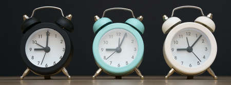 Three small alarm clocks black blue and white show nine oclock, stand on a table on a black...