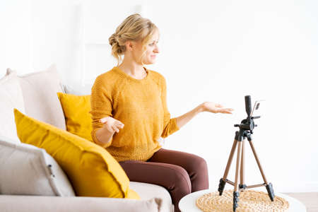 Caucasian blogger Woman using smart phone recording online video in living room at home woman...