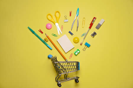 Trolley cart with school supplies on a yellow background. Flat, top view. Back to school concept.の写真素材