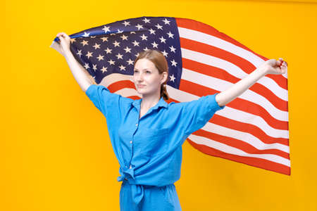 Celebration Independence Day. Stars and stripes. Young woman holding United States America flag isolated on yellow studio background. Looks insanely happy and proud as patriot his country in blue suitの写真素材