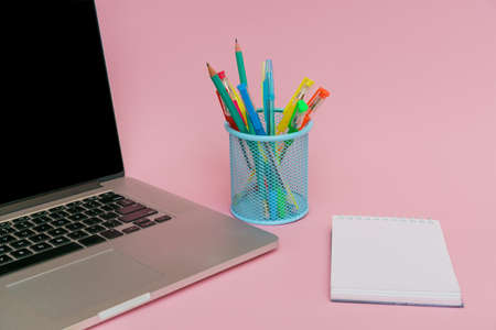 Laptop pens and colored pencils in blue stand and white stickers on pink background, back to school and business education conceptの写真素材