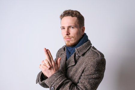 Young man with beard stands on light background with copy space for your advertising shows a gesture...