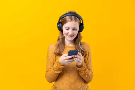 Happy girl communicates via video communication using a mobile phone on a colored background in the studio, Caucasian girl rejoices in communicationの写真素材
