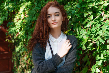 Portrait young tender red haired young girl with healthy freckled skin in white shirt and gray looking at camera with thoughtful expression. Caucasian woman model with ginger hair posing outdoorsの写真素材