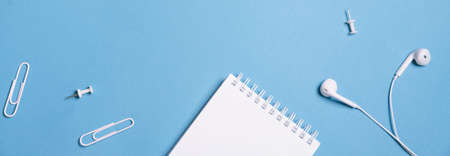 Wired white headphones notepad on a spring clips and buttons on a blue background with copy space