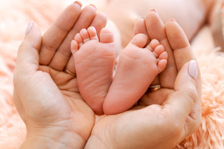 Baby feet in mothers hands. Tiny feet newborn baby on a female hand shape close-up. Mom and her...