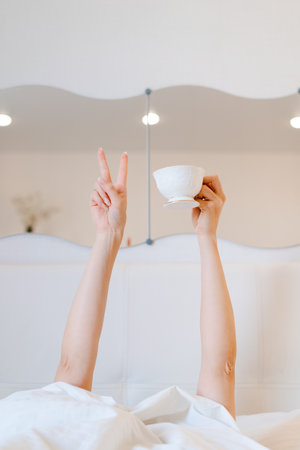 Young woman with a coffee mug in bed with white linens. Minimal happy morning morning concept.