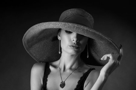 High fashion portrait of an elegant young woman in a black hat and lingerie. Black and white photo,...