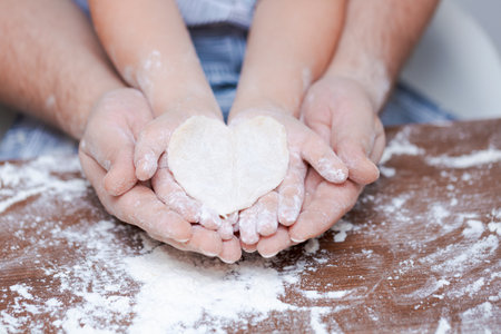 Top view father and childs hand, cut out heart shaped cookies from dough on hands on the background of a wooden table with loose flour. Flat failure.の写真素材