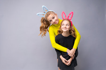Close-up portrait two cheerful pretty young girls with bunny ears in yellow and black sweaters hugging and posing near gray wall. Friends smile and send a kiss. Place for text.の写真素材