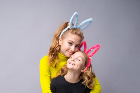 Close-up portrait two cheerful pretty young girls with bunny ears in yellow and black sweaters...