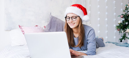 Young woman shopping online for christmas, sit on bed in blue cozy clothes for shopping at home and gifts to friends and relatives for christmas and new year. Winter discountsの写真素材