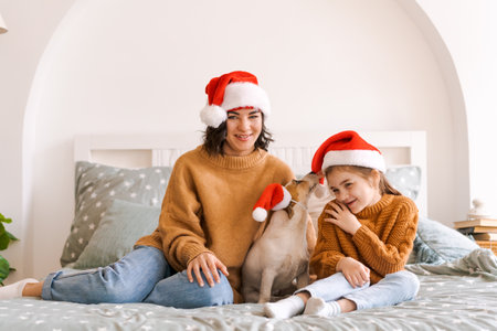 Portrait happy caucasian family in Santa Hats for Christmas with a dog jack russell sit on the bed and have fun, relationship between mom and daughter. New year and christmas conceptの写真素材