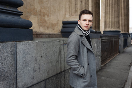 Young man walking down street, autumn or winter cold day. Outdoors, outside. Gorgeous guy in gray...