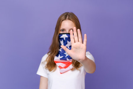 Young beautiful patriotic woman wearing United States flag face mask over purple background with open hand making a stop sign with a serious and confident expression, protection gestureの写真素材