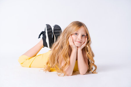 Studio portrait pretty girl with curly hair sitting on floor in studio smiling at camera. In yellow jumpsuit posing caucasian girl model happy smilingの写真素材