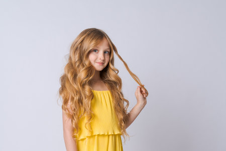 Happy half-length school age girl portrait in yellow clothes with long wavy blond hair smiles sweetly, isolated on light gray background. Caucasian girl modelの写真素材