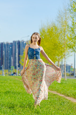 Attractive happy young woman long flowered dress flying her hair enjoying free time outdoors in city against backdrop trees and blue sky. Beauty girl summer portrait. Freedom lifestyle spring conceptの写真素材