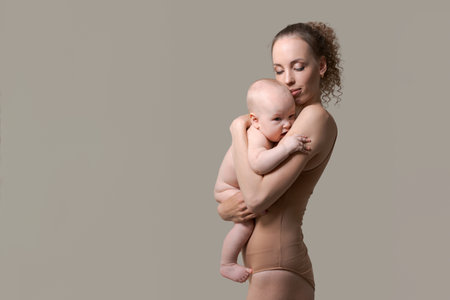 Loving mother hugs and kisses a child, holding him in her arms, in studio on background. Caucasian young woman holding her little son, space for your textの写真素材