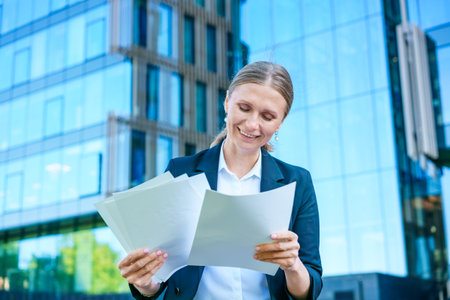 Elegant caucasian business woman in formal wear holds paper documents in her hands on the background of an office office building, an office worker near the business center.の写真素材
