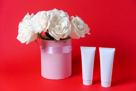 Natural white rose bouquet. Empty white hair shampoo tube with serum bottle and fresh organic roses on red background. Herbal hair care beauty conceptの写真素材