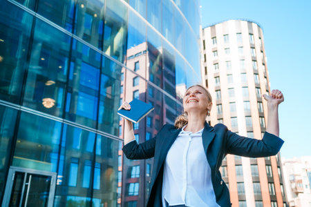 Happy business woman showing thumbs up while standing outdoors against office building background in summer wearing business clothes winner and successful deal friendly smiling, Recommendation conceptの写真素材
