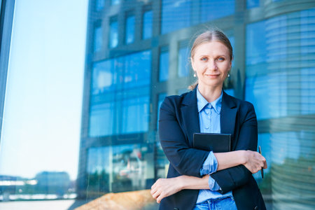 Successful beautiful business woman standing against backdrop buildings writes notes in a notebook or plans a working day in business clothes.の写真素材