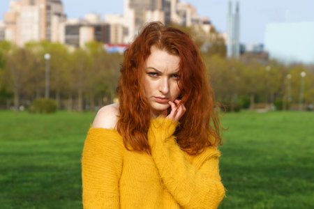 Gorgeous happy redhead woman sitting on beaton and grass relaxing in local park wearing yellow sieve and jeans smiling looking up dreamily spearsの写真素材