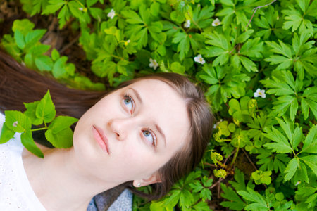 Young woman in casual clothes lies on green, beautiful lawn, dreams in spring. View from above. An attractive lady lies on the grass. Copy spaceの写真素材