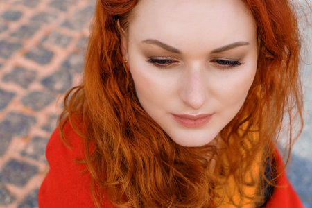 Close-up portrait young caucasian woman with red curly hair in a red coat in the wind develops...