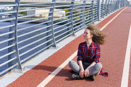 Tired happy woman resting after running, sitting on treadmill and smiling in wind. Summer time....