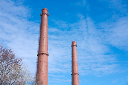 Two tall abandoned industrial chimney pipes against blue sky. Chimneys an industrial plant. Smoke pipes. Smoke tubes. Factory pipes pipes made of bricks.の写真素材