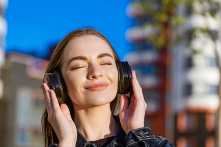 Beautiful young girl listening to music on headphones, street style, outdoor portrait, hipster girl enjoying a sunny day in spring in casual clothesの写真素材