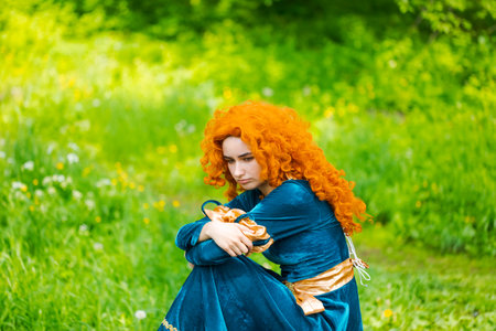Cute girl in beautiful dress in an forest. Character cosplay festival portrait girl with curly long hair against the background of green bushes in a blue dressの写真素材