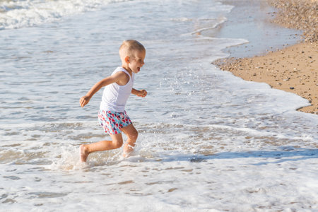 a little boy runs joyfully along the seashore on a sunny summer day, a happy childの写真素材