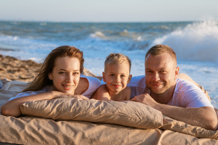 happy family on the beach at sunset lie on a bed on the sand, mom dad and little son. Family and vacation conceptの写真素材