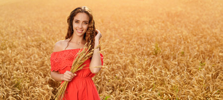 banner of a happy young beautiful smiling woman in a wheat field in a red dress holding spikelets in her handsの写真素材
