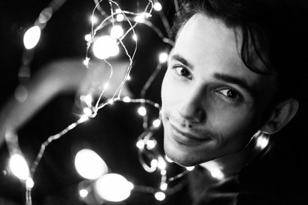 young guy holding glowing garlands at night black and white portrait, selective focus