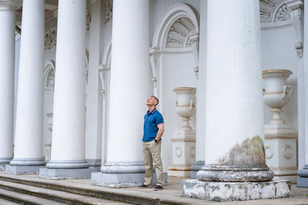 a man in casual clothes stands near the columns of a white buildingの写真素材