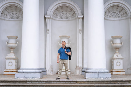 a man in casual clothes stands near the columns of a white buildingの写真素材