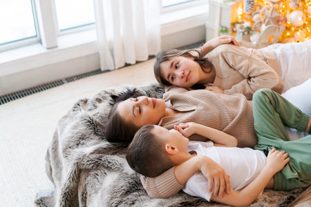 Happy family mom and two kids lying on bed waiting for Christmas and laughingの写真素材