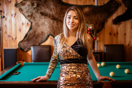 woman in gold and black dress stands in front pool table. She is smiling and she is enjoying herself