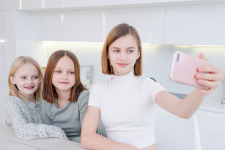 girl is taking picture of her two younger sisters. The girls are smiling and seem to be enjoying the moment. The photo captures a happy and loving family momentの写真素材